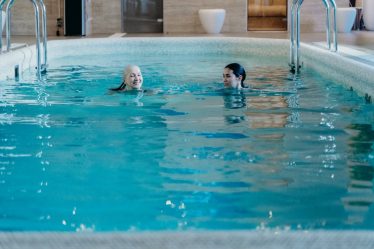 Senior woman and adult woman enjoying a relaxing swim in an indoor pool, featuring leisure and relaxation.